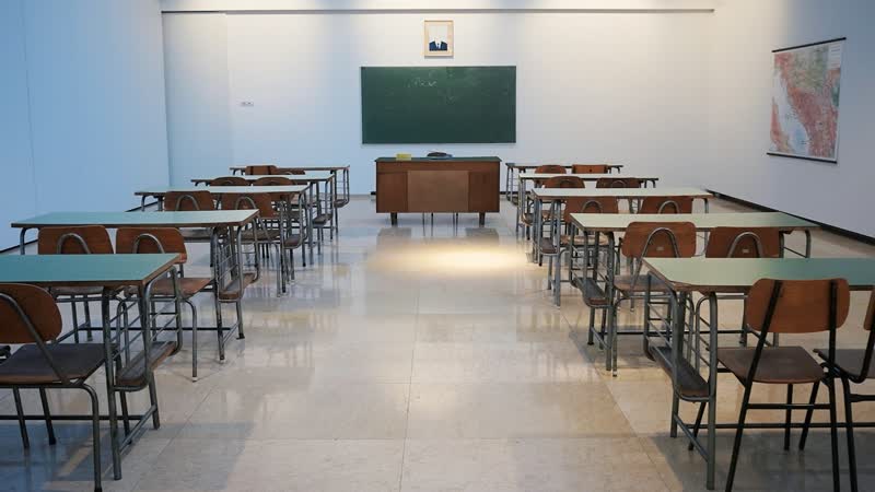 Empty classroom with rows of desks facing a chalkboard and a teacher’s desk.