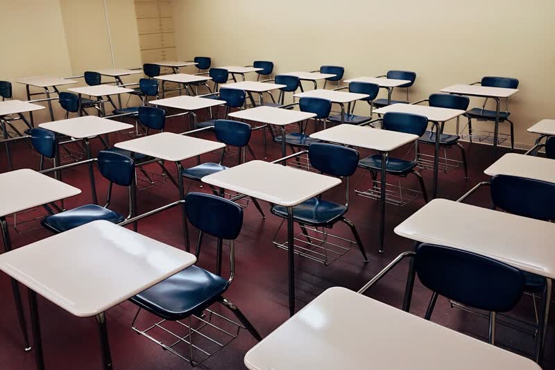 An empty classroom of white desks and blue chairs on a red floor.