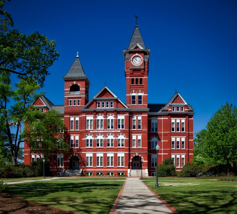 A red-brick school building with a clock tower and a tree-lined walkway.